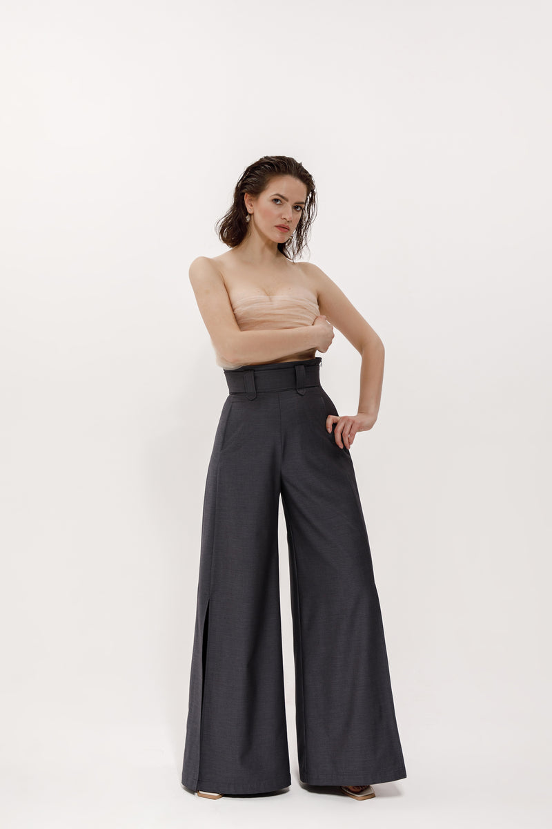 A woman dressed in elegant palazzo pants with slits and pockets, made with thin wool in dark gray color